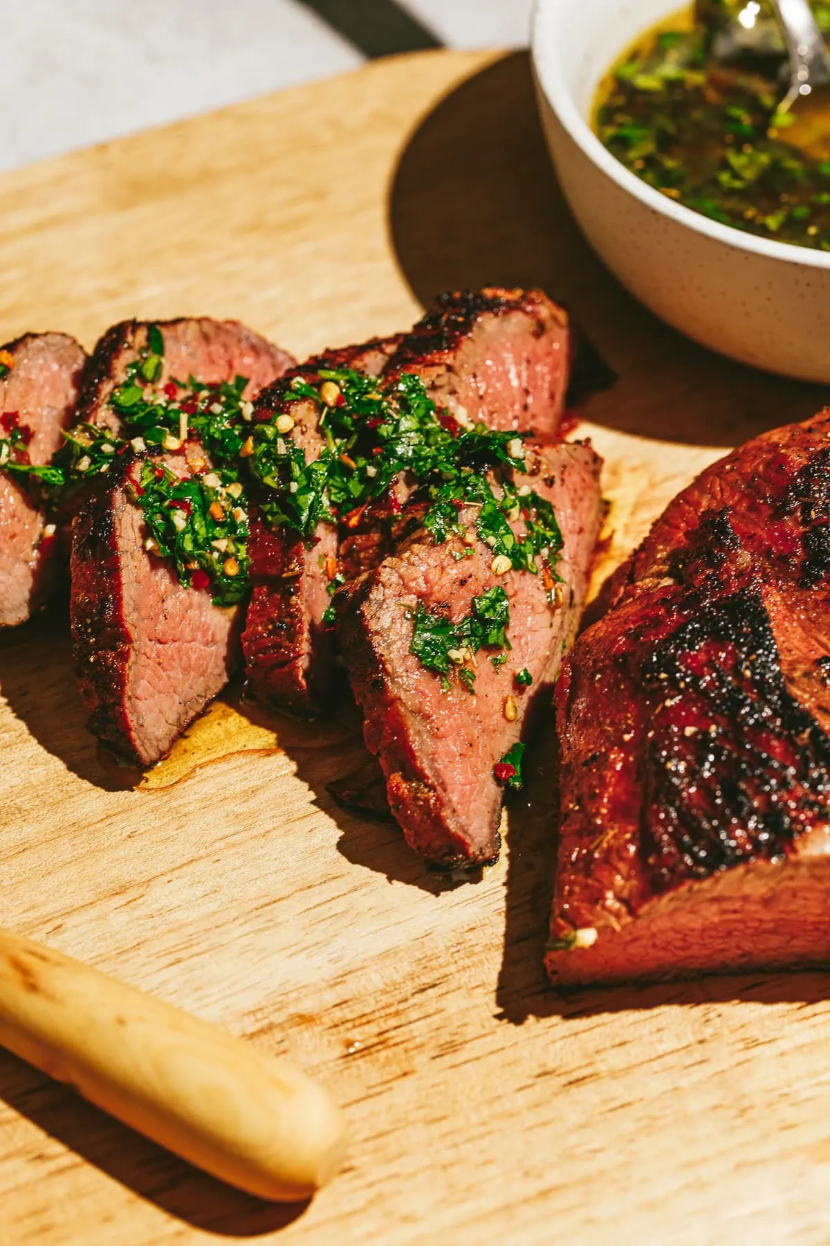 Sliced Traeger tri-tip on a cutting board topped with chimichurri.