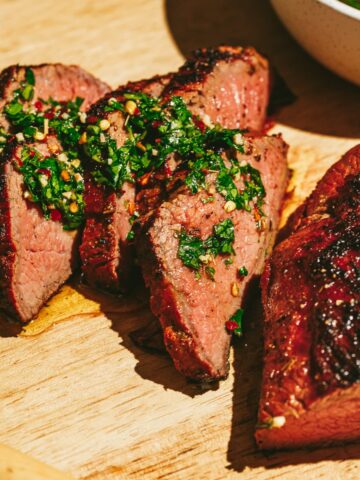 Slices of tri-tip on a cutting board topped with chimichurri.