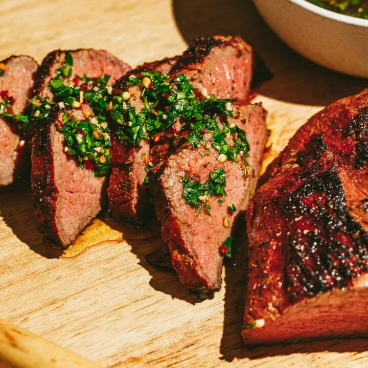 Slices of tri-tip on a cutting board topped with chimichurri.