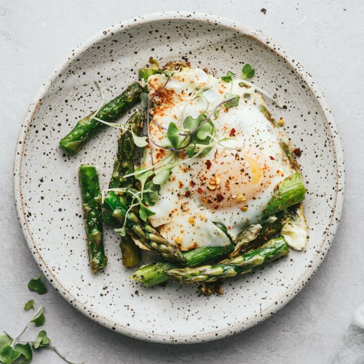 Asparagus and eggs on a plate with seasonings and microgreens.