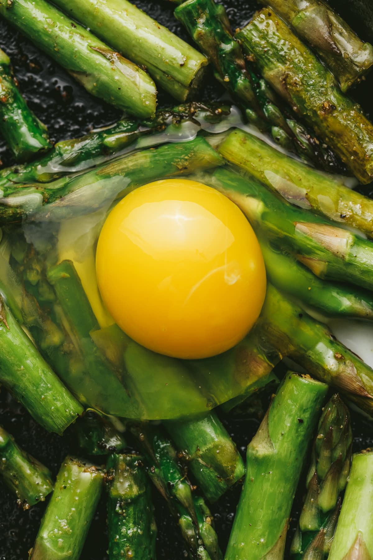 A raw egg on top of cut asparagus spears.