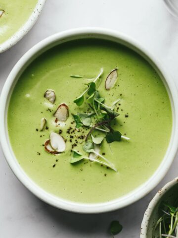 A bowl of broccoli almond soup with sliced almonds and microgreens as garnish.