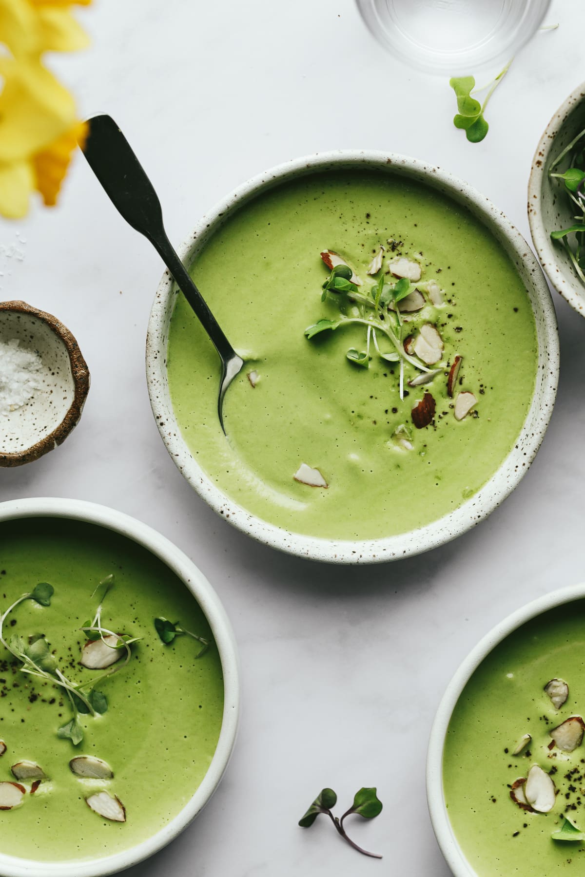Bowls of broccoli almond soup on a white marble backdrop.