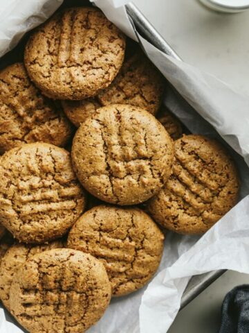 Almond flour peanut butter cookies in a square tin with a glass of milk.
