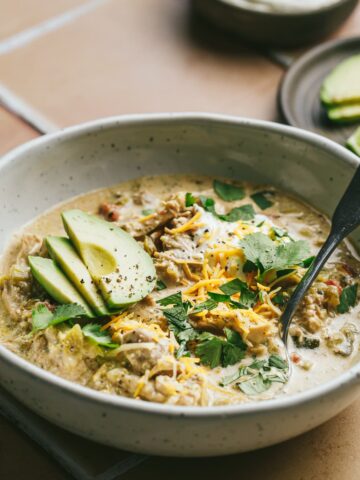 Crockpot green chicken chili in a bowl with a spoon and garnishes.