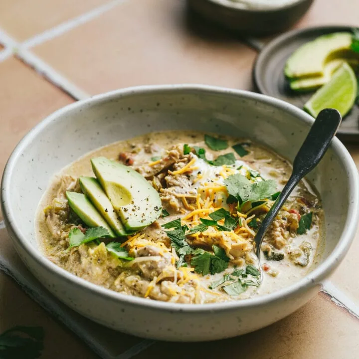 Crockpot green chicken chili in a bowl with a spoon and garnishes.
