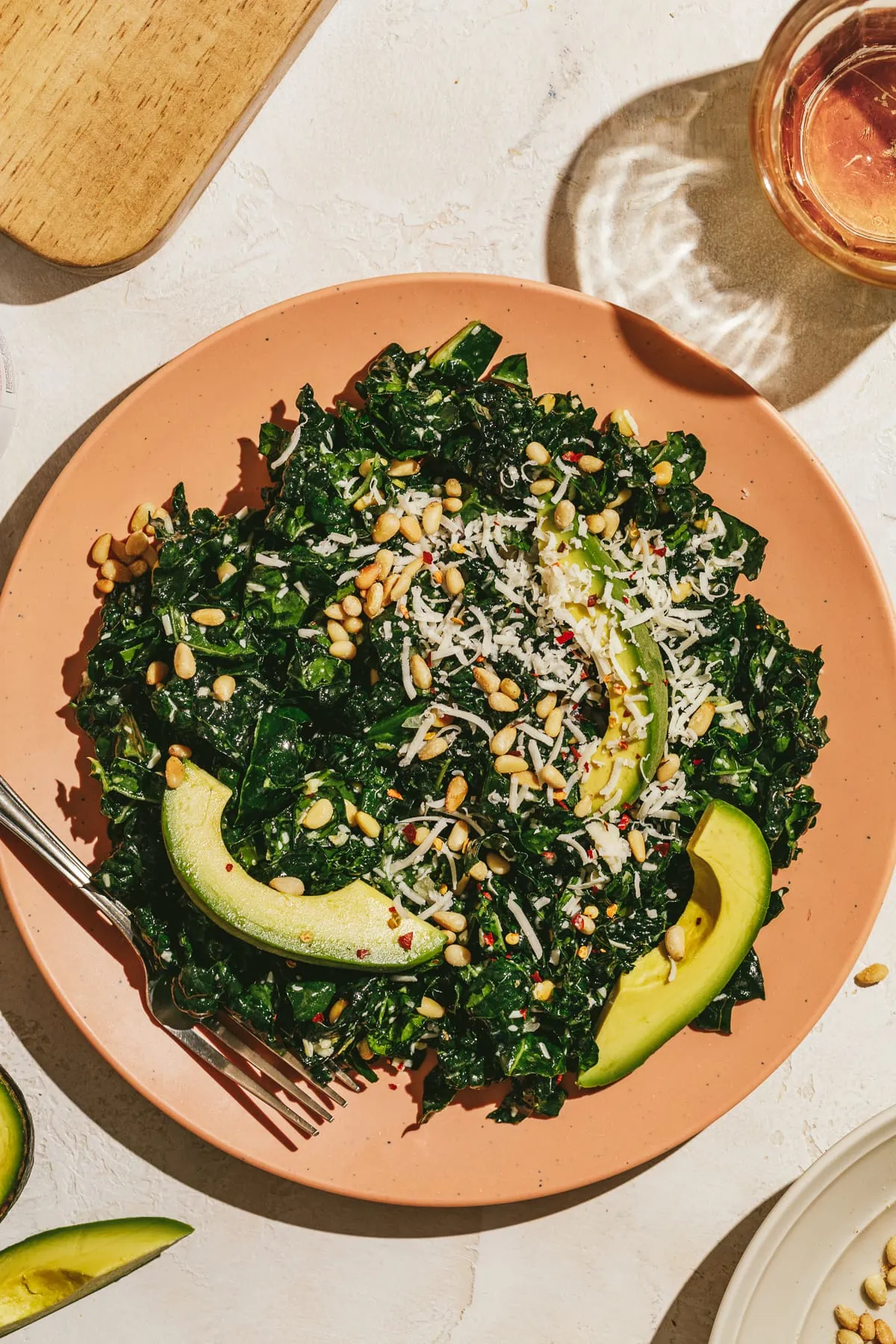A Tuscan kale salad on a pink plate topped with avocado.