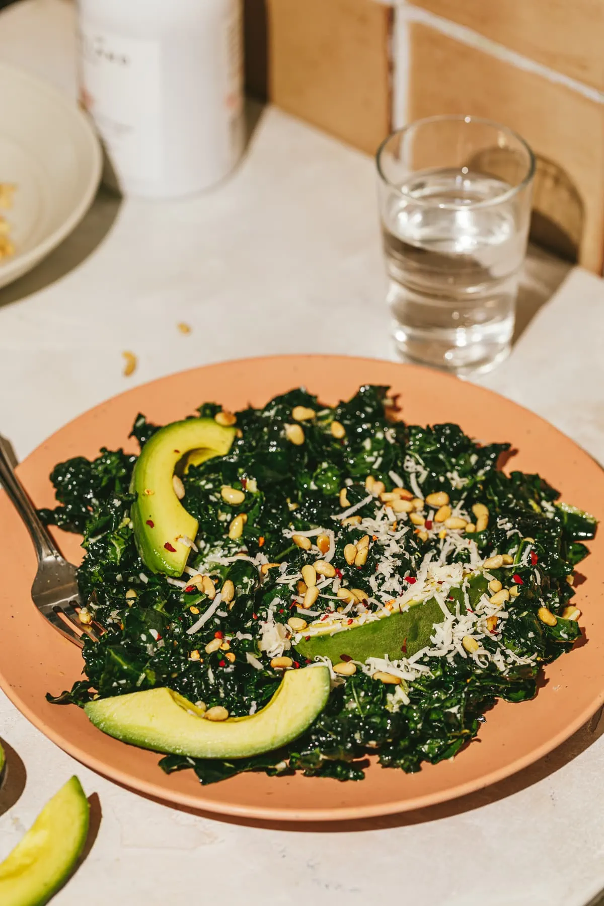 Tuscan kale salad on a pink plate with avocado and cheese.