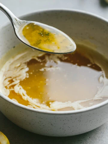 A spoonful of garlic butter sauce over a white bowl.