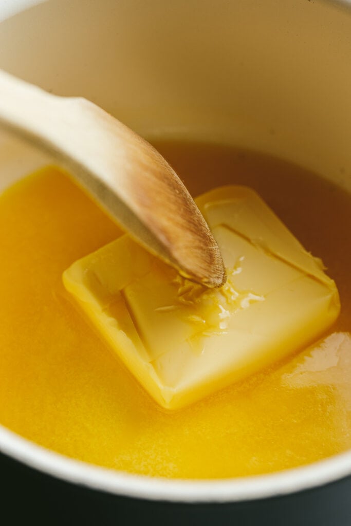 A wooden spoon stirring melting butter in a saucepan.