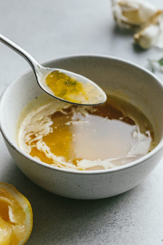 A spoonful of garlic butter sauce over a bowl with it.