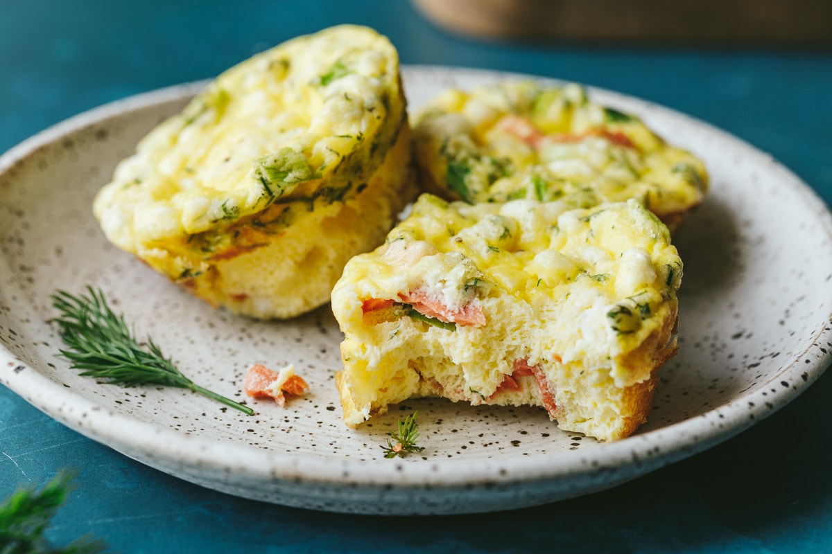 Three keto egg bites with smoked salmon and fresh dill on a white speckled plate.