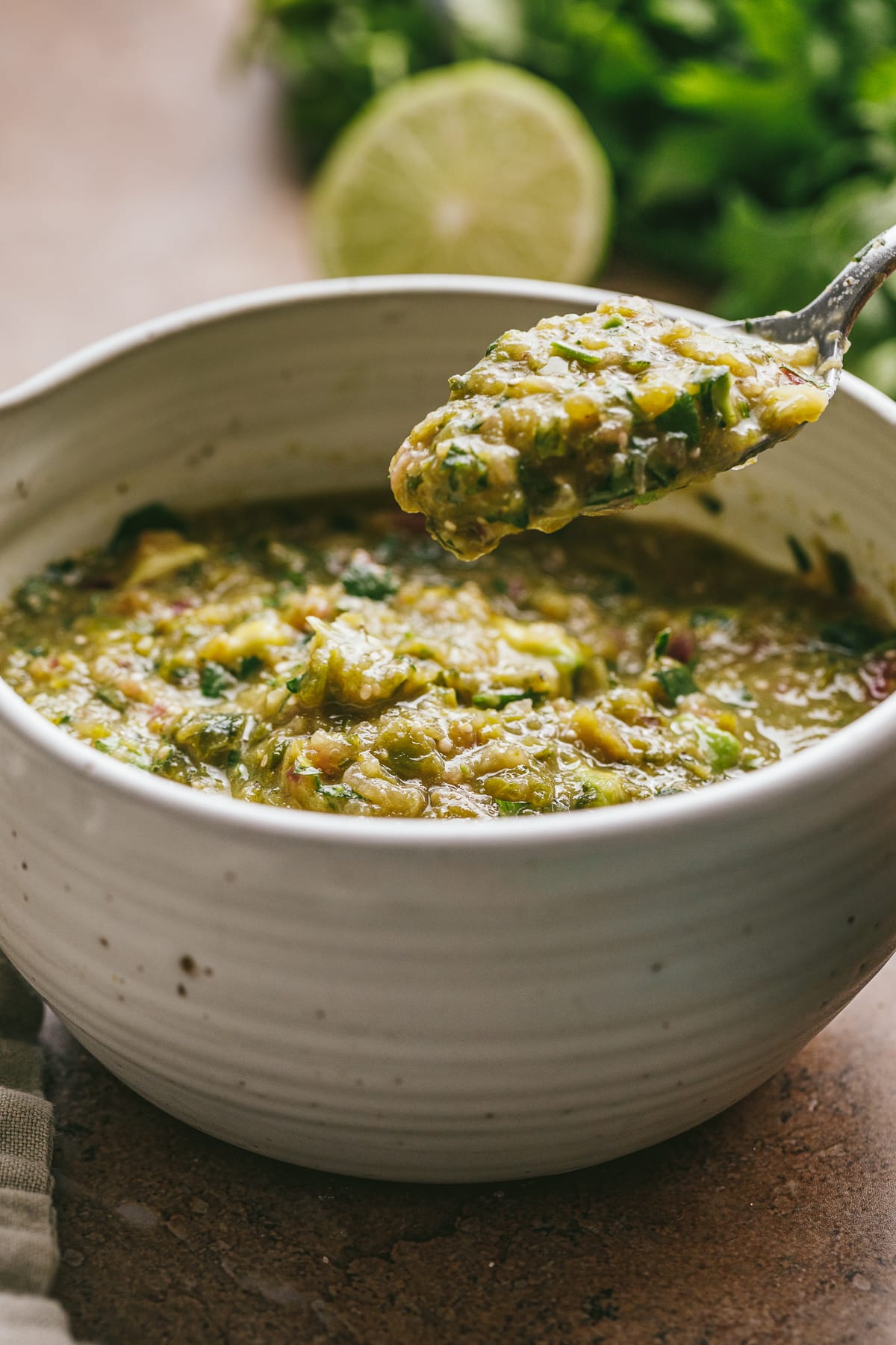 A spoonful of tomatillo green chili salsa from a white bowl.