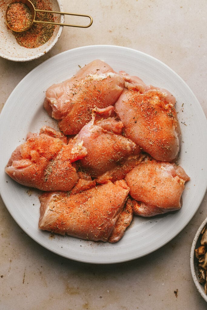Raw chicken thighs with seasonings on a plate.