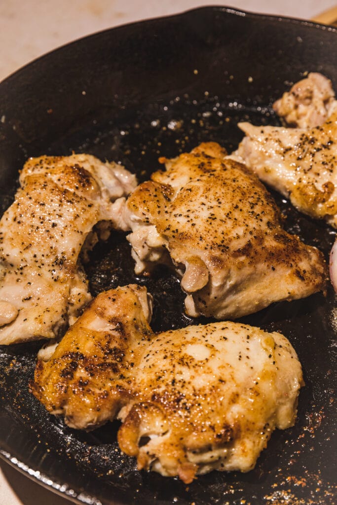 Chicken thighs browning in a cast iron skillet.