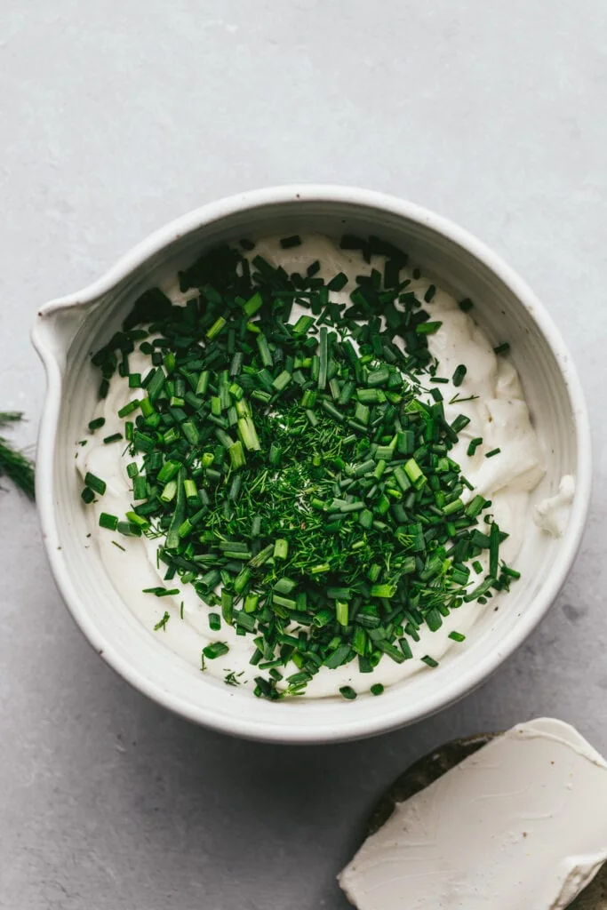 A mixing bowl with chopped herbs and cottage cheese.