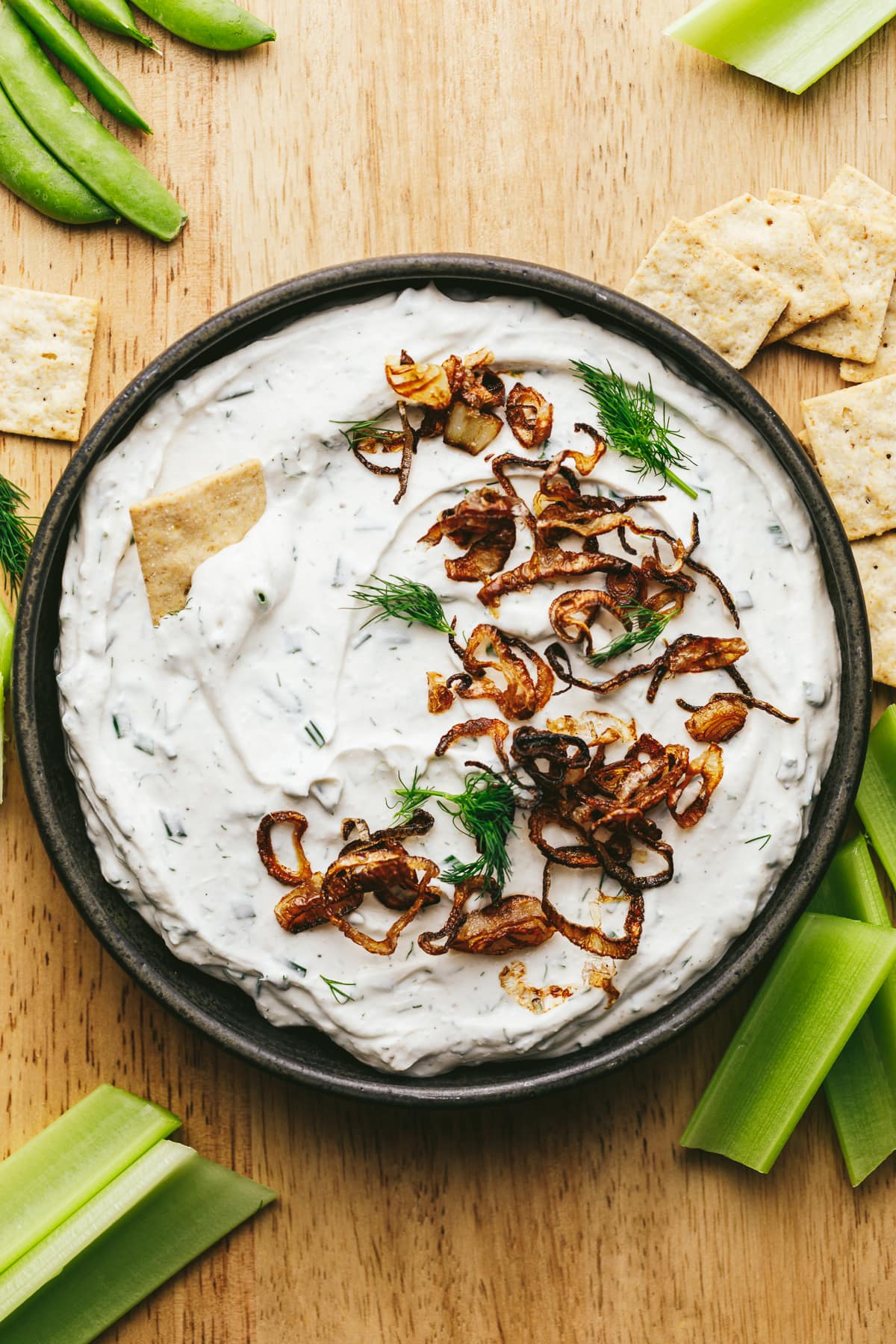Cottage cheese dip with crackers and veggies on a cutting board.