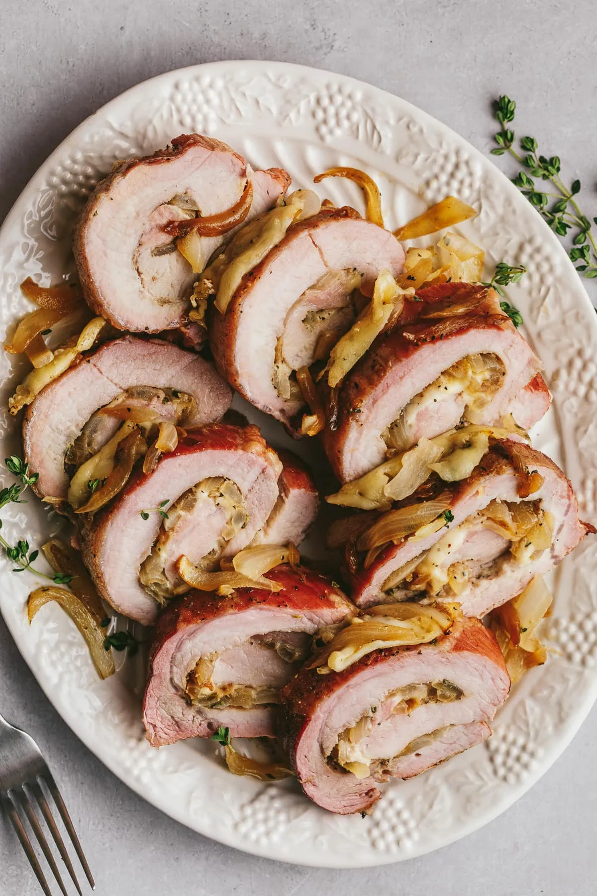 A serving platter with sliced smoked pork loin and fresh thyme as garnish.