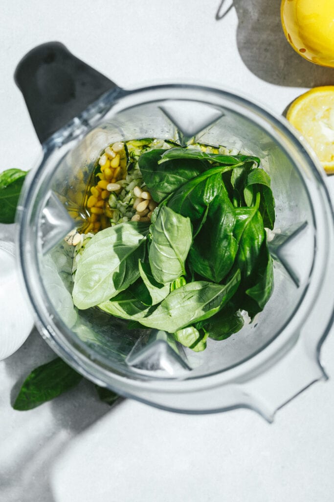 Ingredients for zucchini pesto in a high-speed blender with lemon next to it.