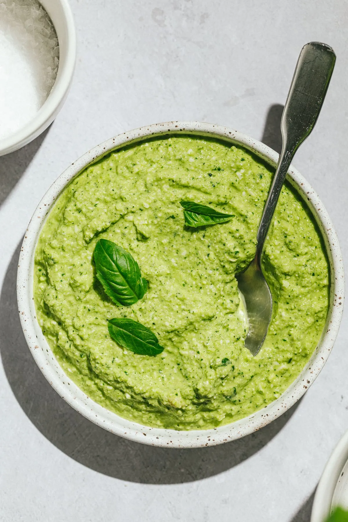 Zucchini pesto overhead shot with a serving spoon and basil leaves.