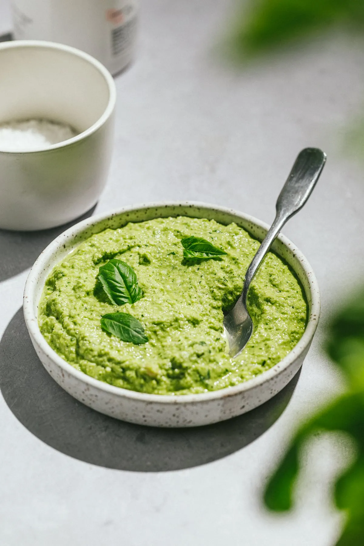 Zucchini pesto in a bowl with a spoon and basil leaves as garnish.