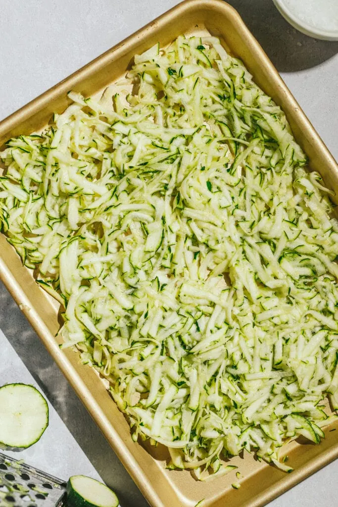 Shredded zucchini on a baking sheet for zucchini pesto recipe.