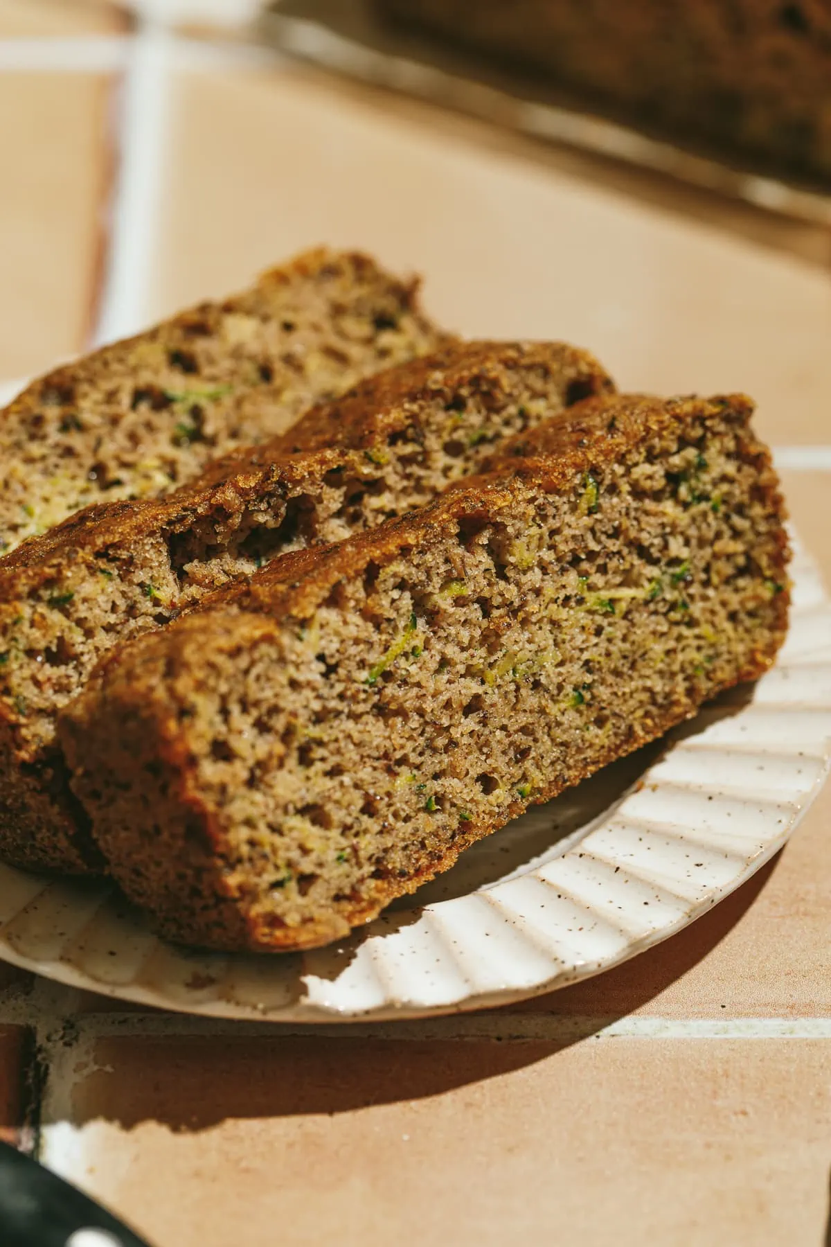 Closeup of three slices of keto zucchini bread on a ribbed edge plate.