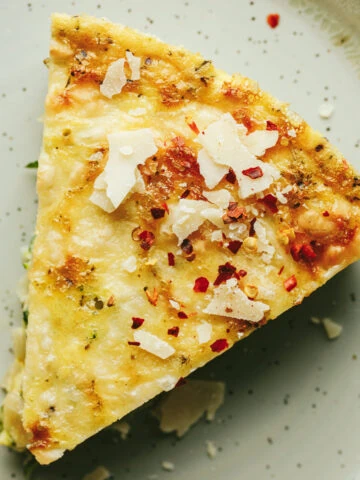 Closeup of a slice of crustless zucchini quiche topped with parmesan cheese and red pepper flakes.