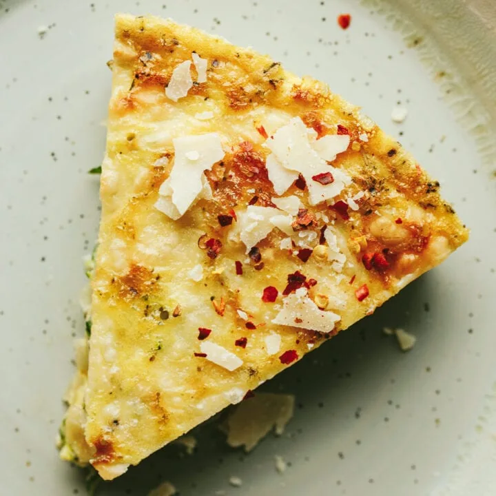 Closeup of a slice of crustless zucchini quiche topped with parmesan cheese and red pepper flakes.