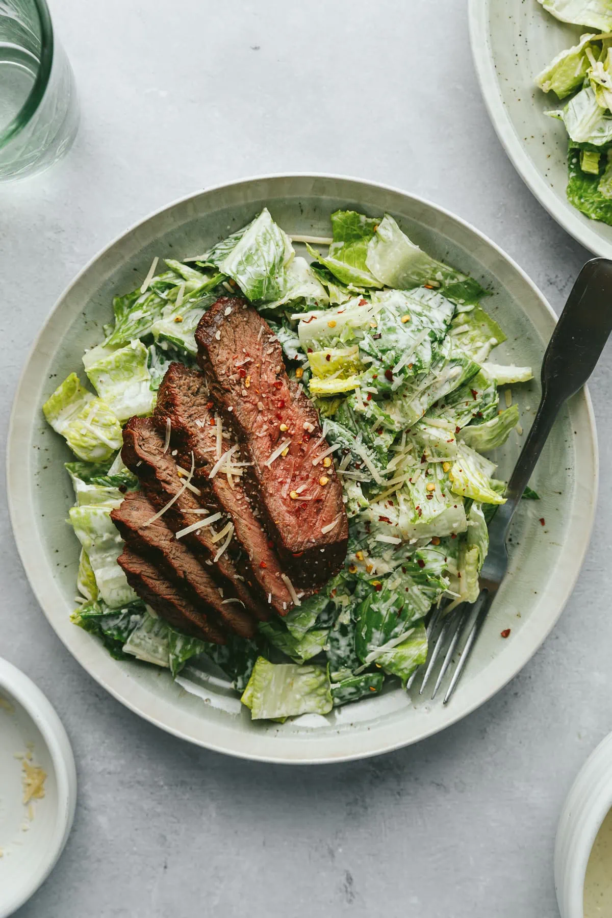 Steak Caesar salad on a green plate with a green glass next to it.