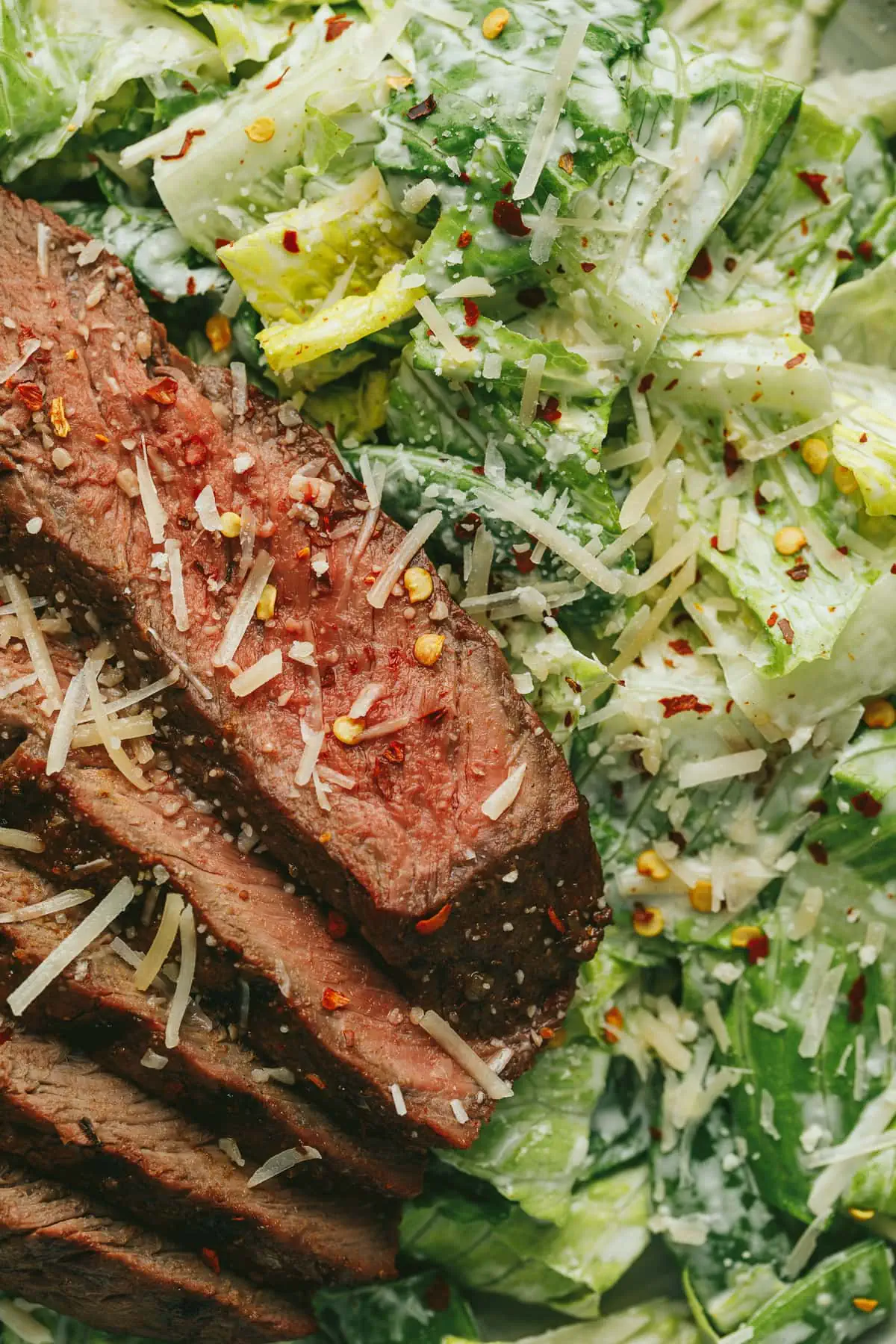 Closeup of steak slices on top of Caesar salad.