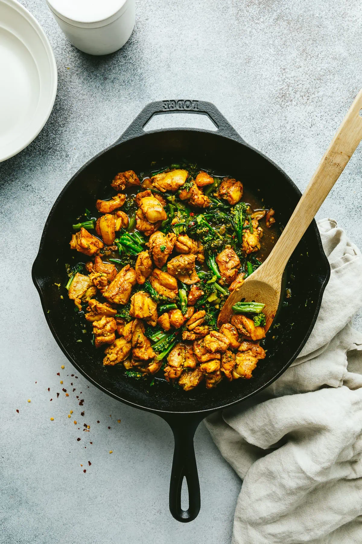 Black cast iron skillet with turmeric black pepper chicken and a wooden spoon.