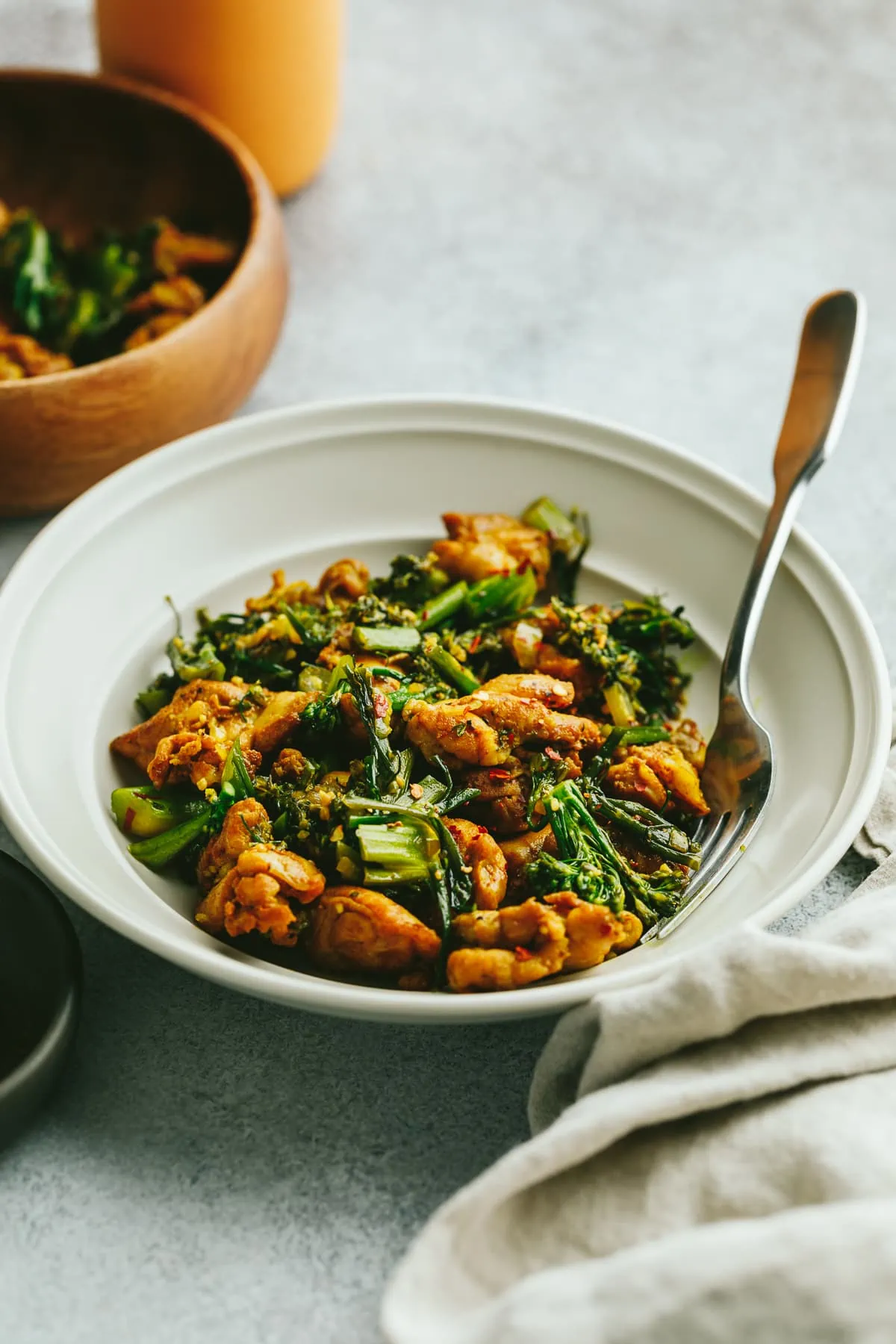 A bowl of turmeric and black pepper chicken with a wooden bowl behind it.