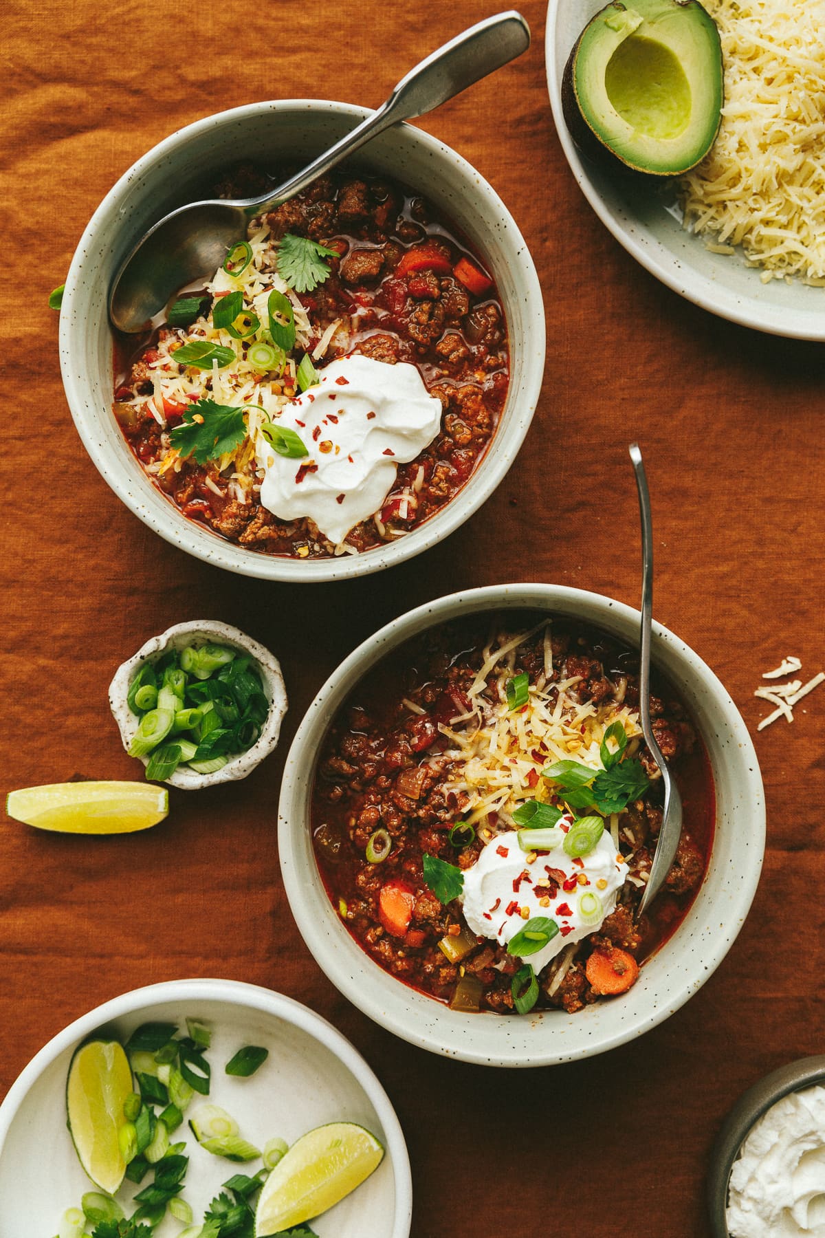 Two bowls of slow cooker no bean chili with toppings next to them on an orange tablecloth.