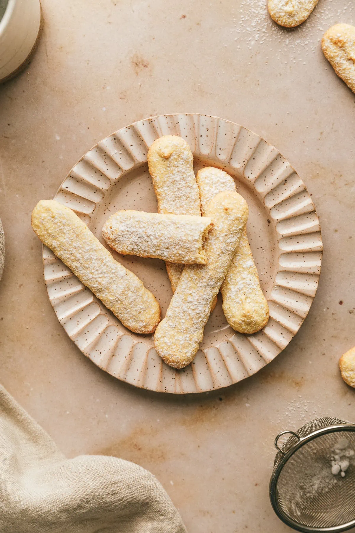 Five sugar-free ladyfingers on a rimmed plate on a beige marble surface.