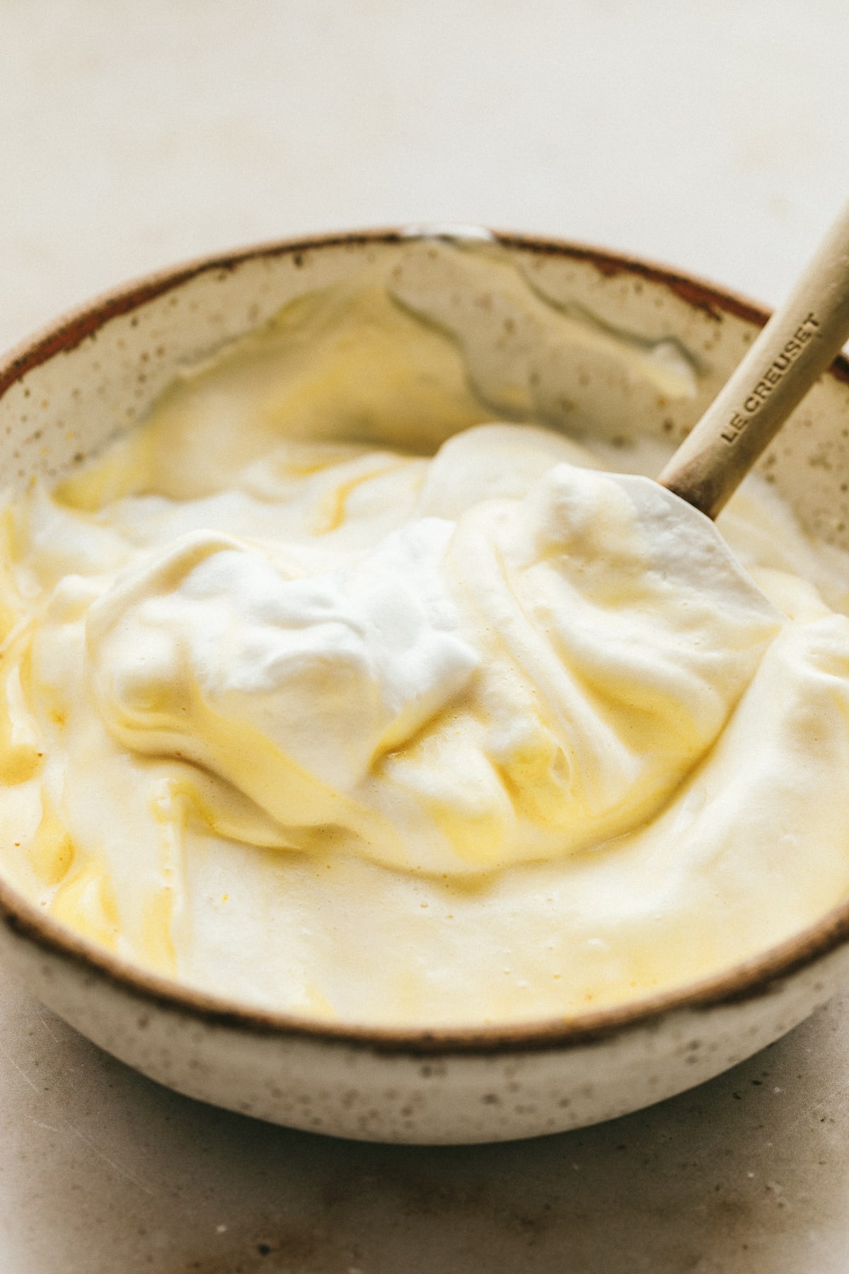 Egg whites in a bowl with yolk mixture and a spatula.