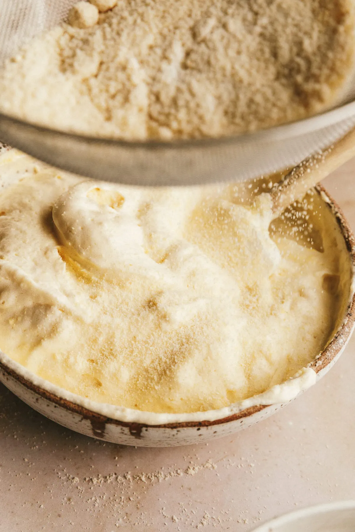 Sifting almond flour mixture over bowl of egg whites to make sugar free ladyfingers.