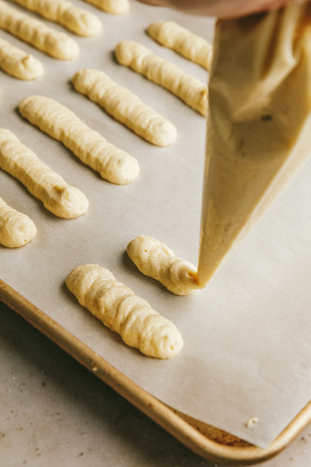 Piping sugar free ladyfingers batter into rows.