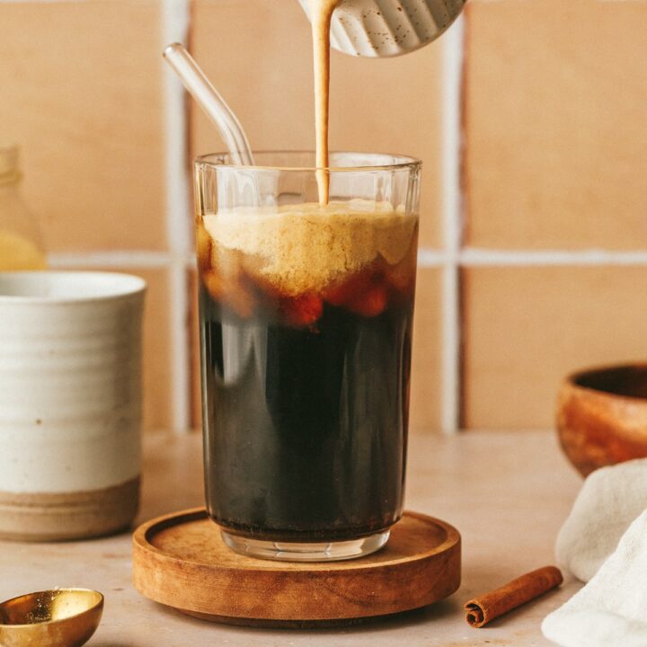 Pouring keto pumpkin spice creamer into a glass of iced coffee.
