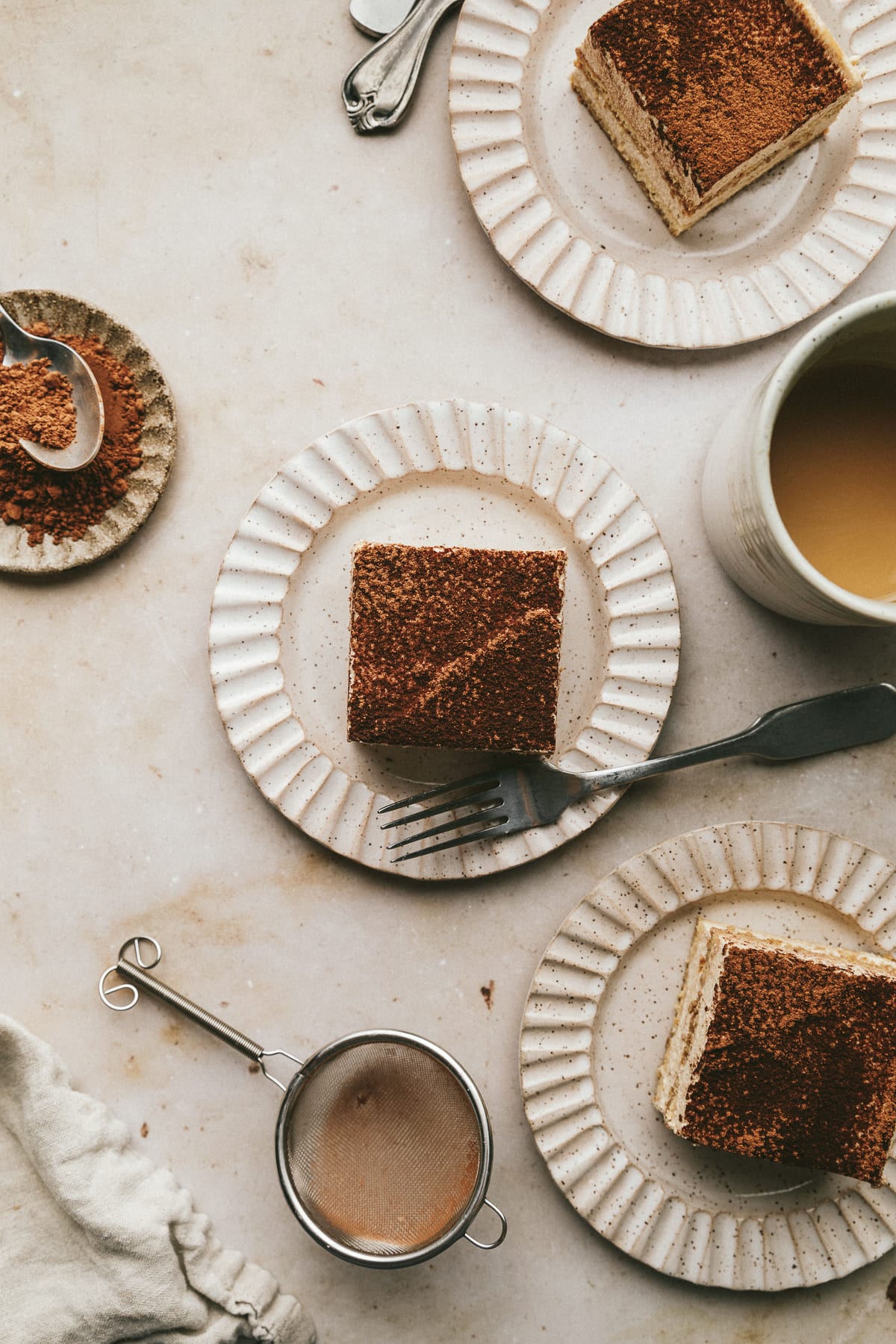Flat lay of ribbed plates with slices of sugar-free tiramisu on a marble surface.