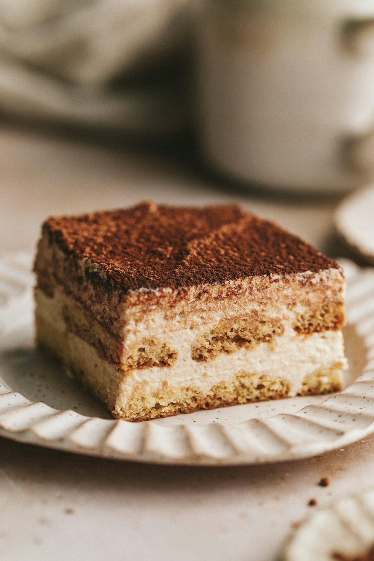 Closeup of a slice of keto tiramisu with a cup of coffee behind it.