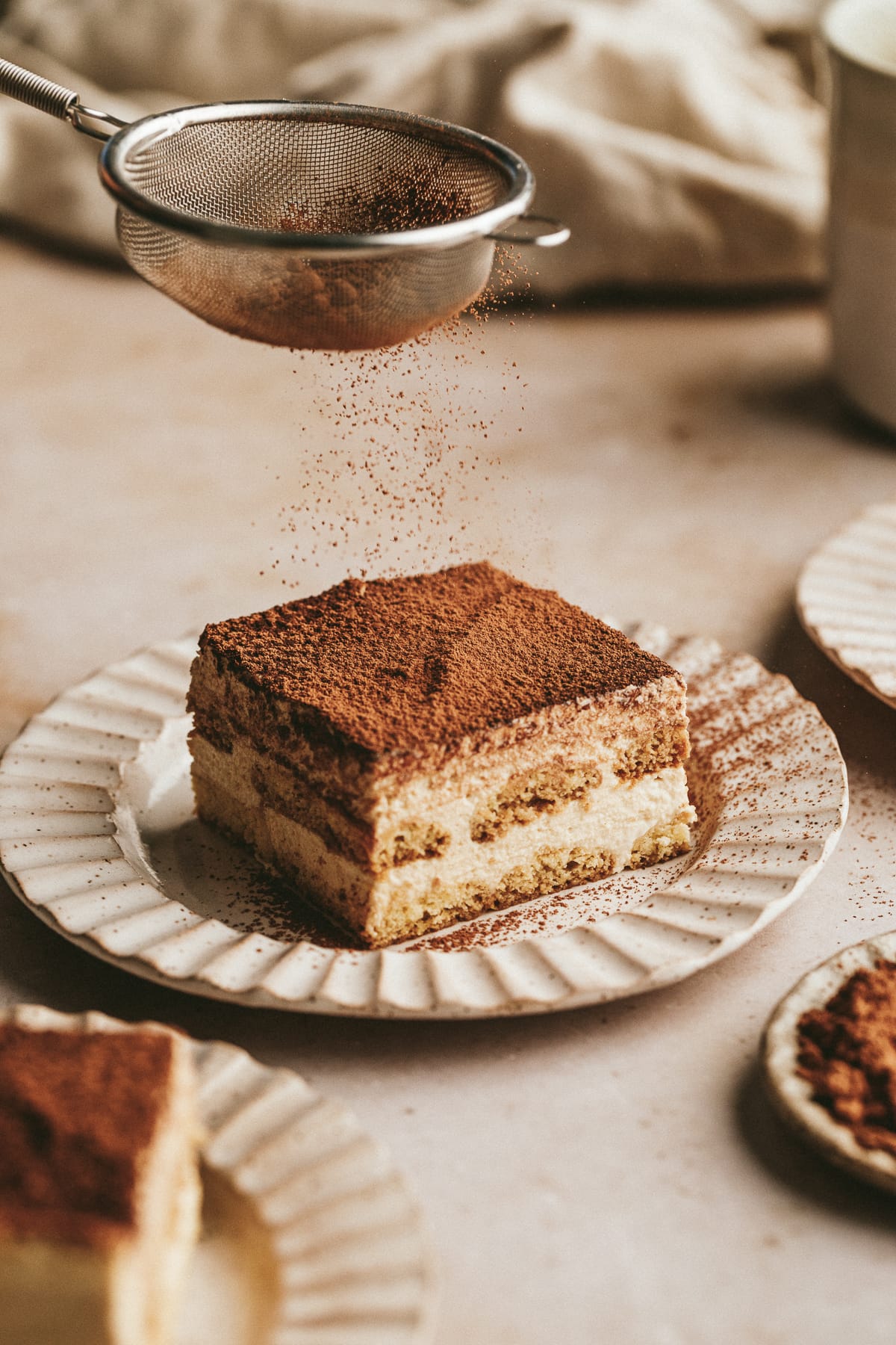 Dusting cocoa powder on a slice of keto tiramisu.