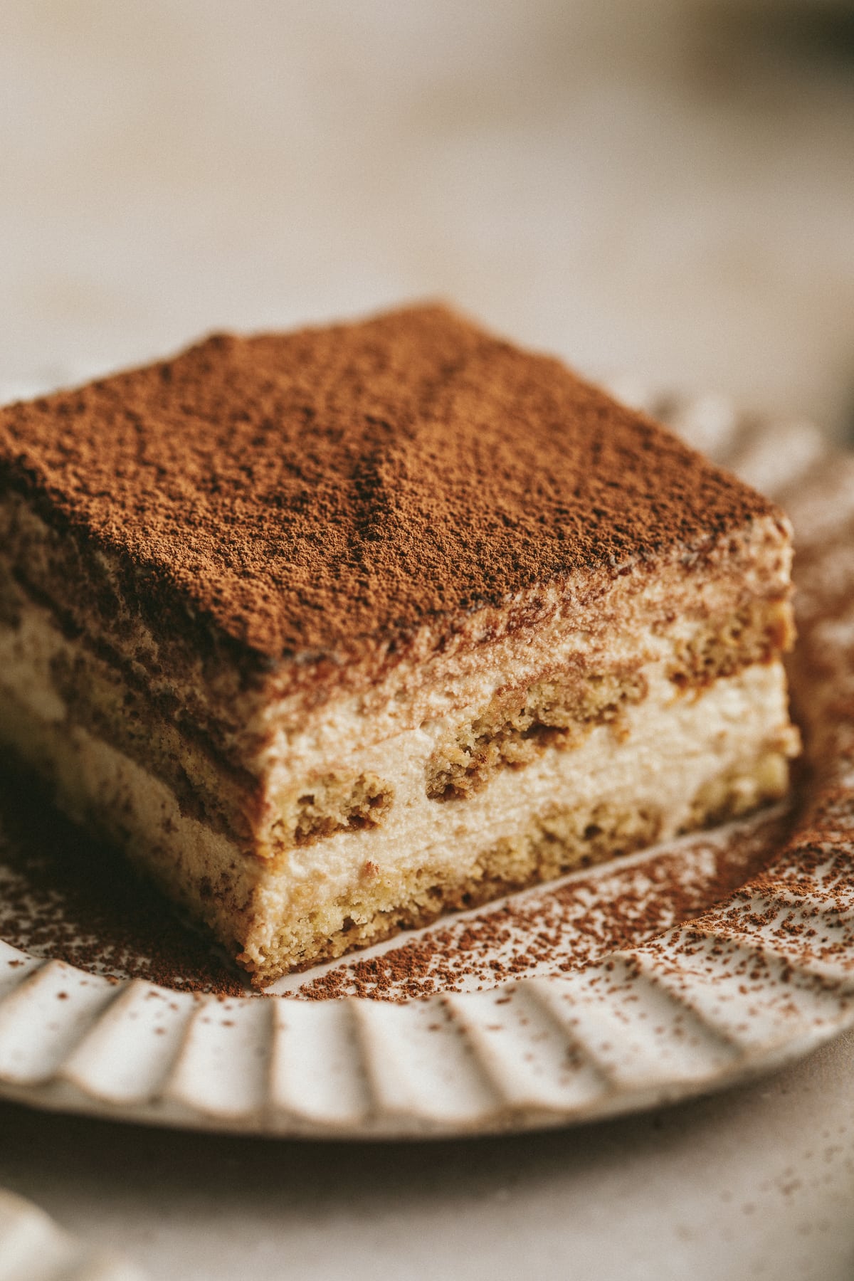 A slice of keto tiramisu on a ribbed ceramic plate with cocoa powder dusted on top.