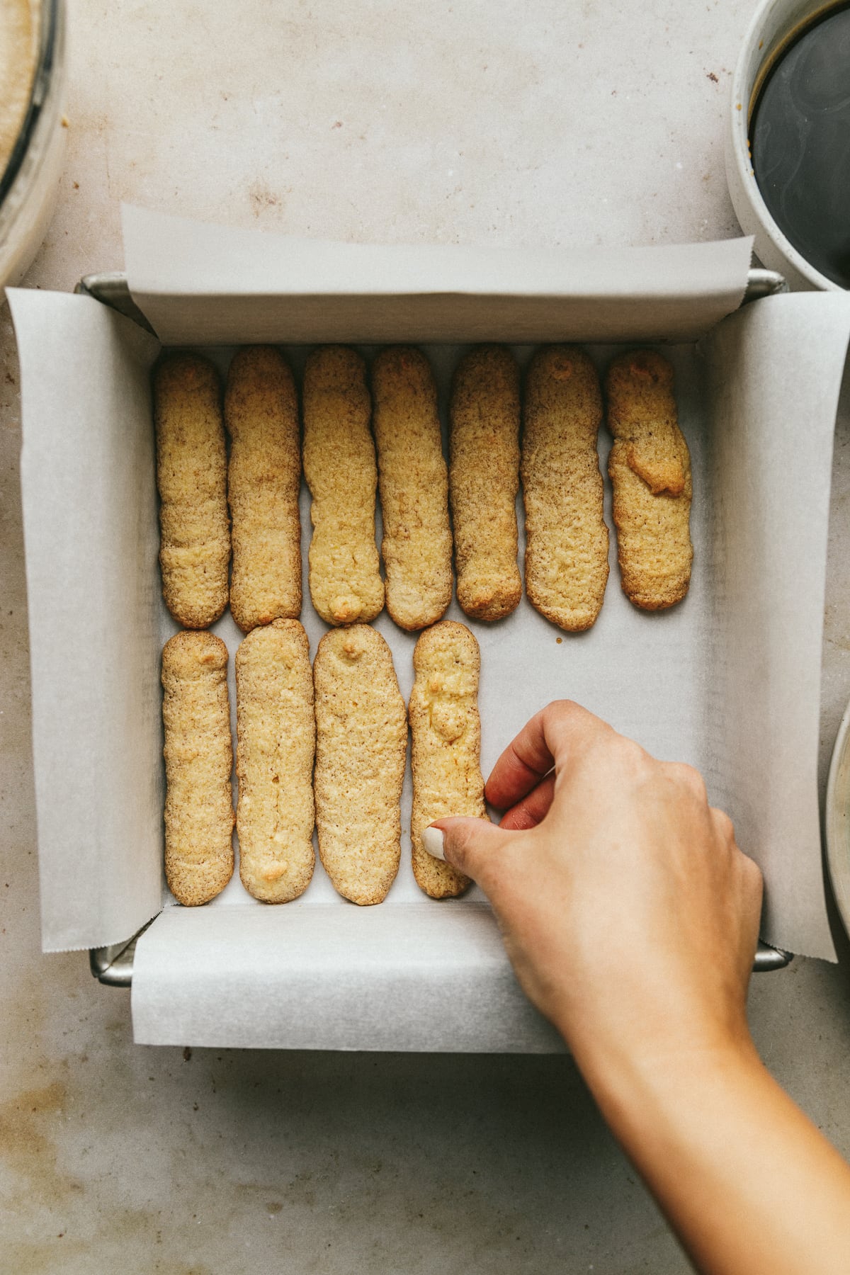 Placing coffee-soaked sponge cookies in a baking dish for keto tiramisu recipe.