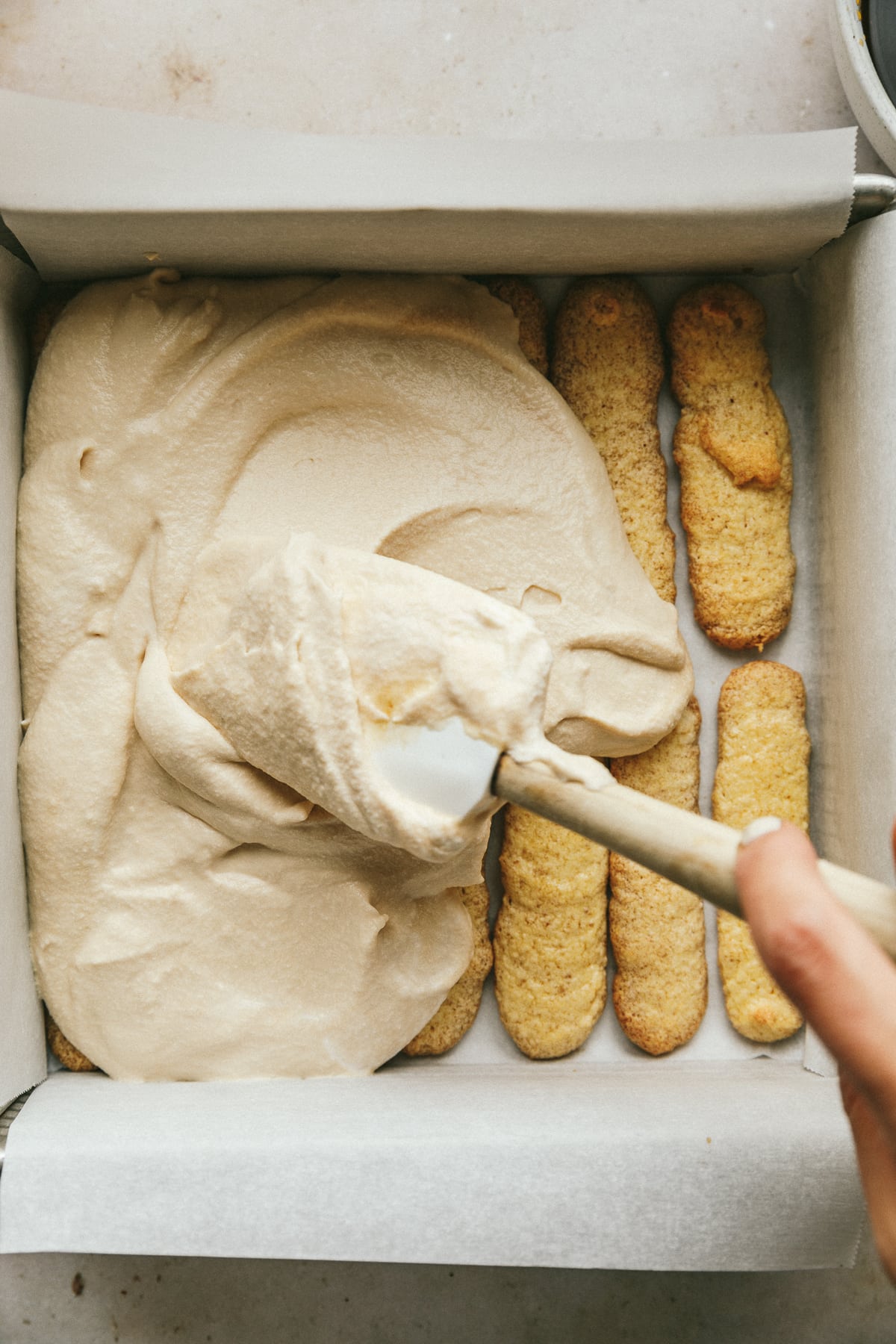 Spreading mascarpone mixture over keto ladyfingers for sugar-free tiramisu.