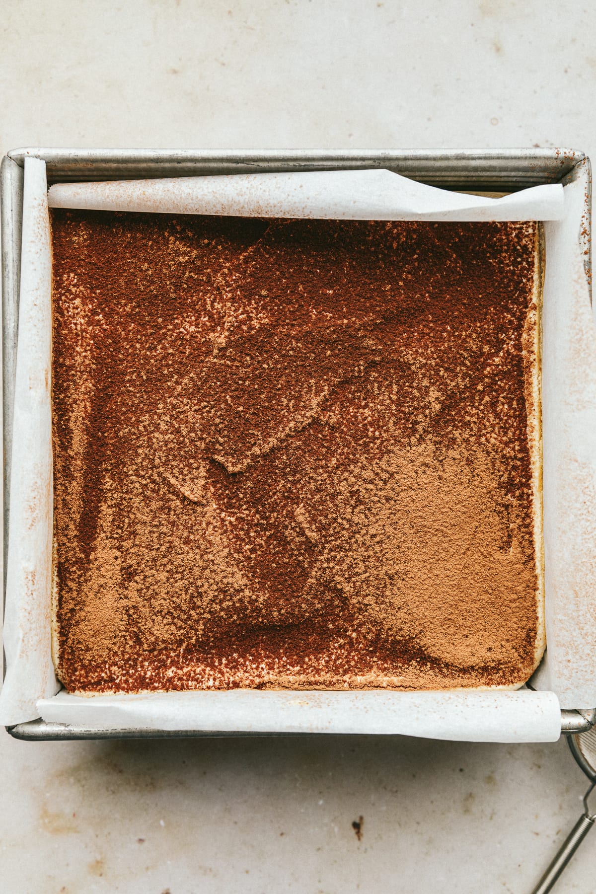 Keto tiramisu in a baking dish with cocoa powder on top.