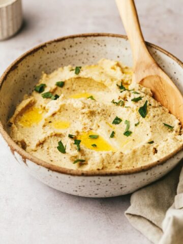 A serving bowl of roasted mashed cauliflower with a wooden serving spoon.