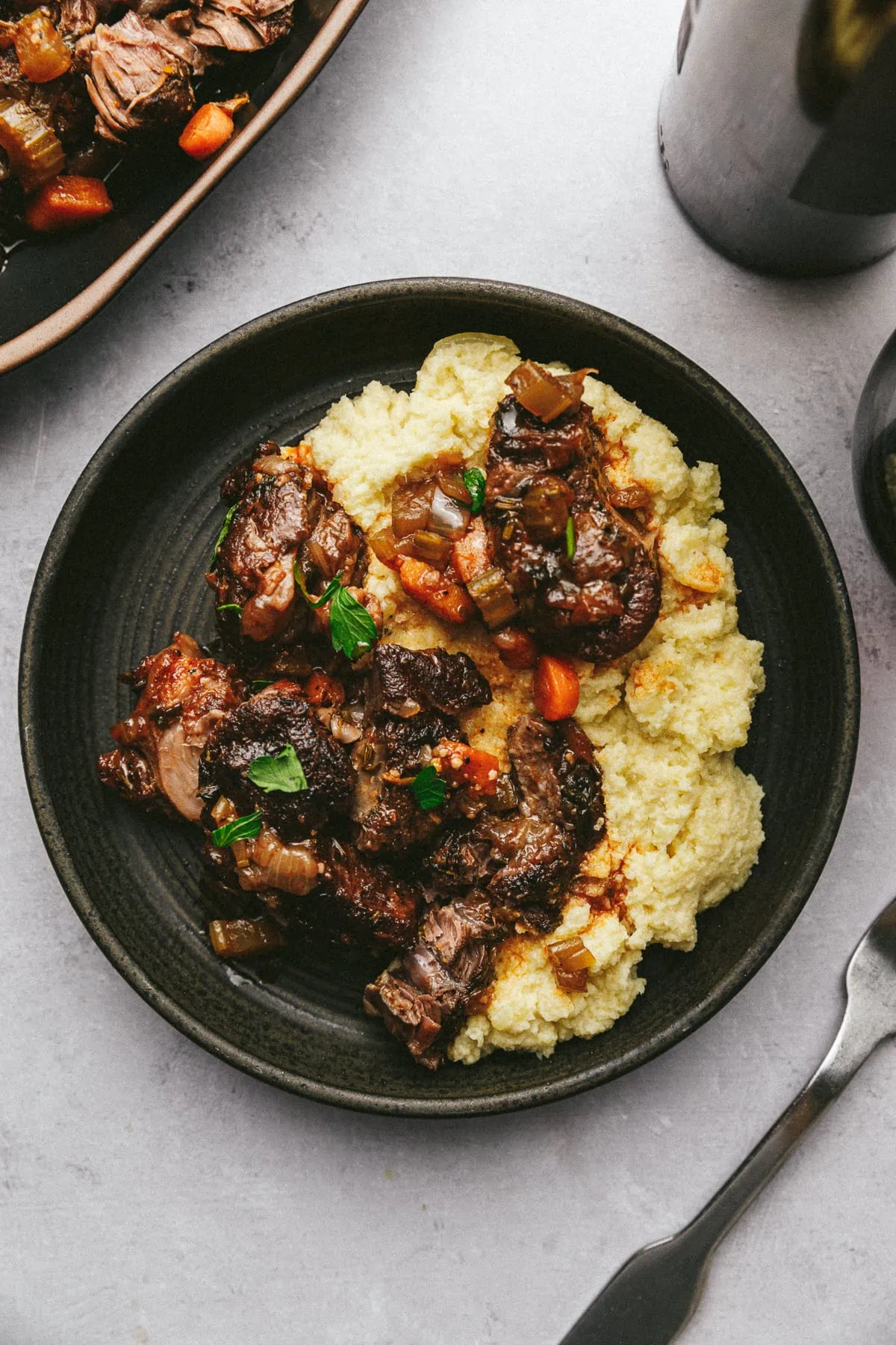 Braised beef shanks on cauliflower mash on a black ceramic plate with a fork.