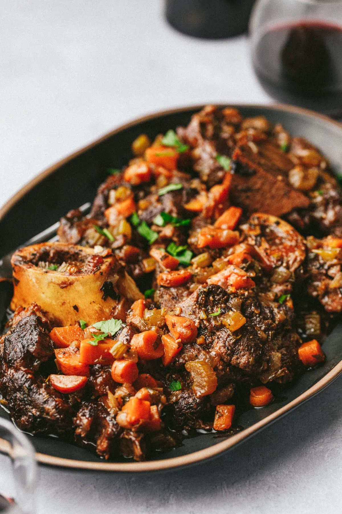 A serving platter with braised beef shanks and a glass of wine in the background.