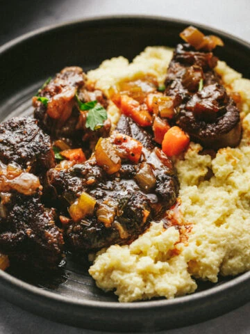 A plate with braised beef shanks and carrots over cauliflower mash.